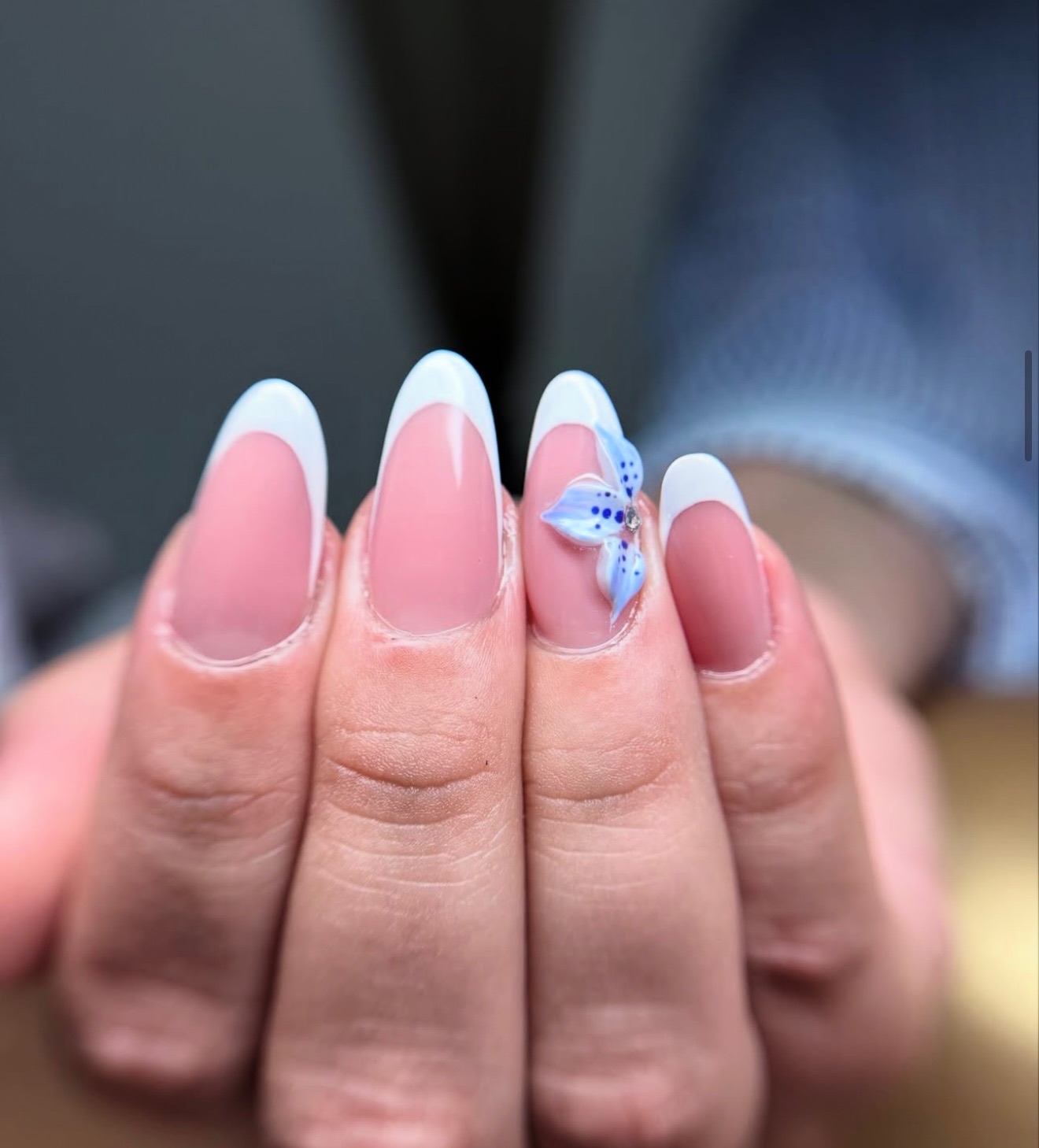 Une main avec une manucure française, avec de longs ongles en forme d'amande ; l'un des ongles est décoré d'une fleur bleue.
